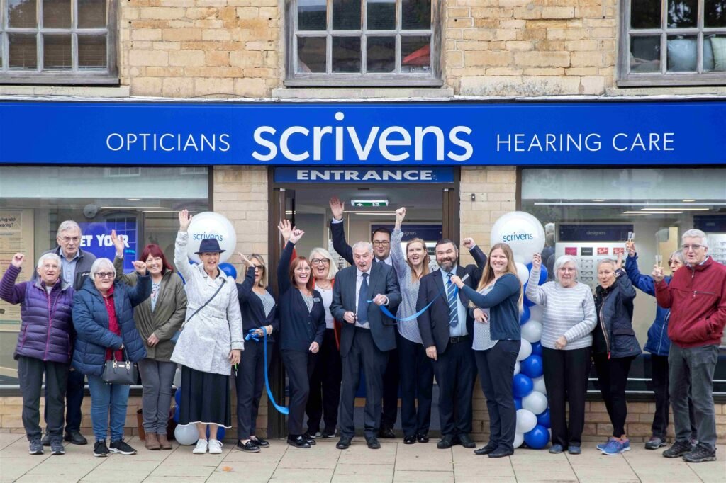Ken Taylor in the centre with staff and customers outside the relocated Scrivens branch in Market Deeping, with blue and white balloons and a ribbon